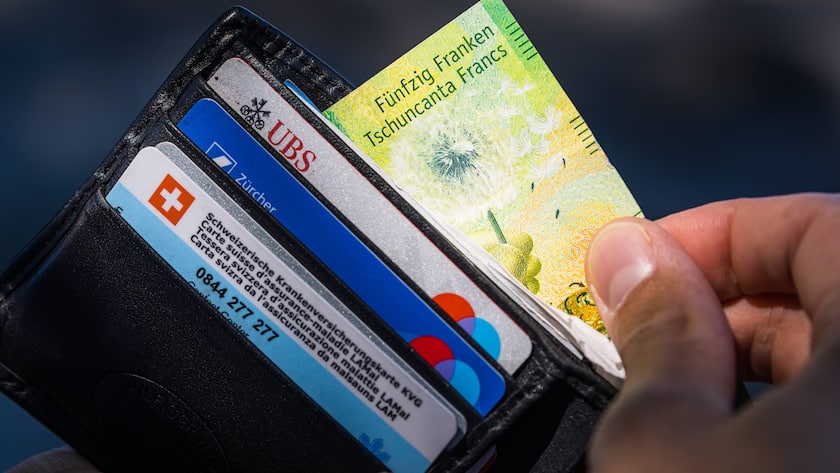 Ein junger Mann zieht eine Banknote mit dem Wert von fünfzig Schweizer Franken aus der Geldbörse. Auch die Debitkarten der UBS und ZKB dürfen in einem zeitgemässen Geldbeutel nicht fehlen. Romanshorn, Schweiz, 02.07.2022