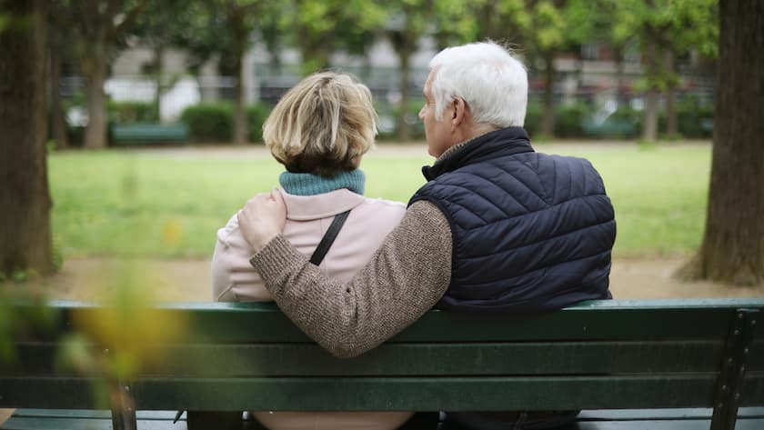 An elderly couple sitting on a public bench in a public garden