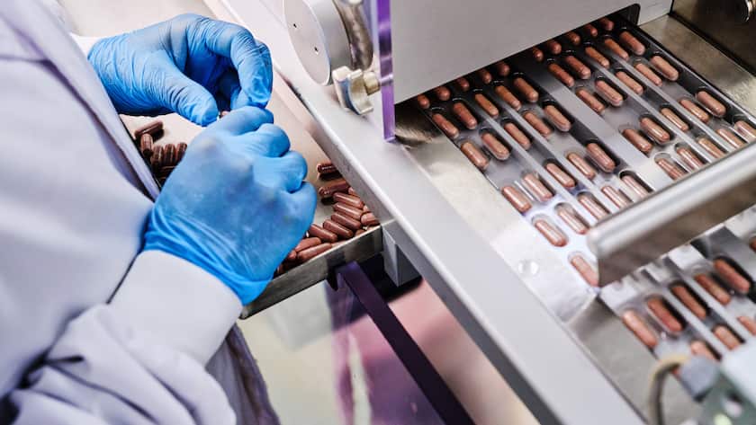 Fabrikarbeiterin in Uniform bei der Bedienung eines Förderbandes mit Tabletten in einem pharmazeutischen Produktionslabor