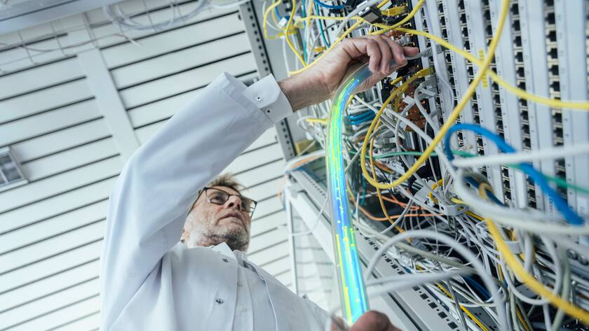 Mature male IT support plugging in fiber optic cable at data center model released Symbolfoto property released LIFIF00013