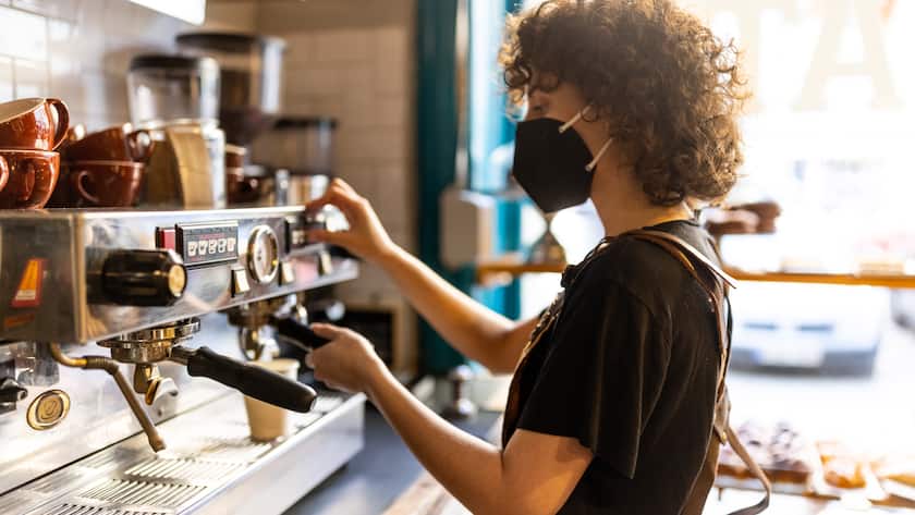 Genderqueer barista wearing a protective ffp2 face mask in a bakery preparing a hot drink