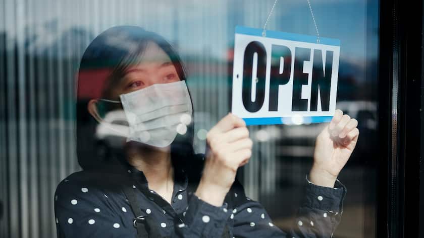 Eine Frau bringt an ihrem Geschäft ein "Open"-Schild an.
