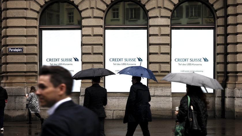 People holding umbrellas walk past screens of Swiss bank Credit Suisse with the words "Part of the UBS Group" at Zurich's Paradeplatz on Monday, June 3, 2024 in Zurich, Switzerland. (KEYSTONE/Michael Buholzer)