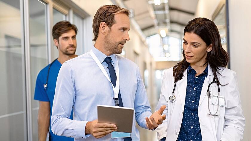 «BGMehrwert» – hier tauschen sich Gesundheitsbetriebe aus Man and woman doctor having a discussion in hospital hallway. Doctor discussing patient case status with his medical staff after operation. Pharmaceutical representative showing medical report.