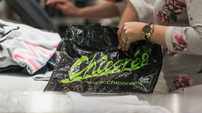 Eine Verkäuferin packt Einkäufe in einen schwarz-grünen Chicorée Sack.