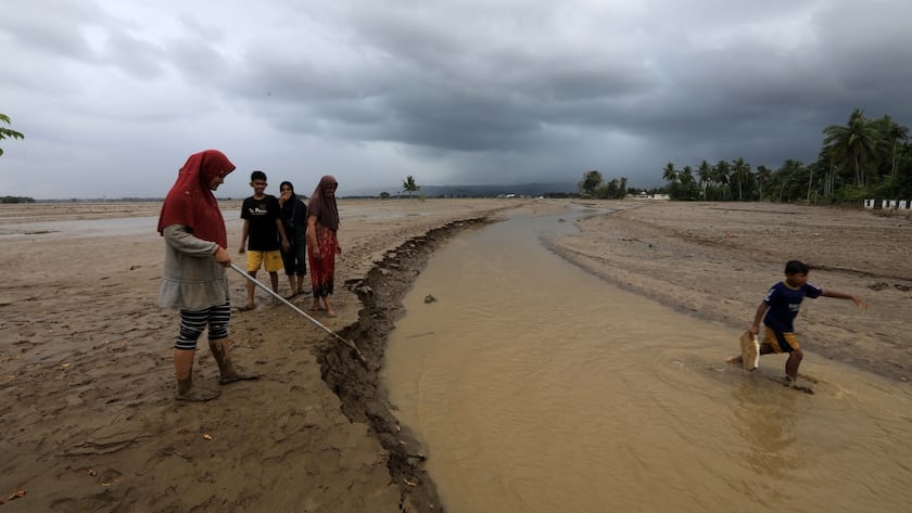Menschen laufen in einem offenen, mit Schlamm und Wasser bedeckten Gebiet in einem von Überschwemmungen betroffenen Dorf in der Region Meureudu, Pidie Jaya, Aceh, Indonesien, am 2. Dezember 2025.