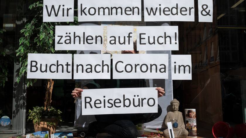 23.03.2020, Nordrhein-Westfalen, Dortmund: Ein Mitarbeiterin eines Reisebüros klebt einzelne Blätter mit der Aufschrift ·Wir kommen wieder & zählen auf Euch! Bucht nach Corona im Reisebüro· in das Schaufenster. Ansammlungen mit mehr als zwei Personen sind bundesweit verboten, Geschäfte und Gastronomiebetriebe geschlossen. Foto: Bernd Thissen/dpa +++ dpa-Bildfunk +++ (KEYSTONE/DPA/Bernd Thissen)
