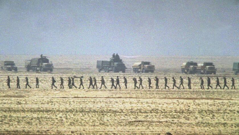FILE - In this Sunday, February 24, 1991 file photo, a line of captured Iraqi soldiers are marched through the desert in Kuwait past a group of U.S. Marine Second Division vehicles after the ground offensive got underway during the Persian Gulf War. In February 1991, after months of building an international coalition, U.S. forces entered Kuwait to end the Iraqi occupation of its smaller, oil-rich neighbor. (AP Photo/Sadayuki Mikami, File)