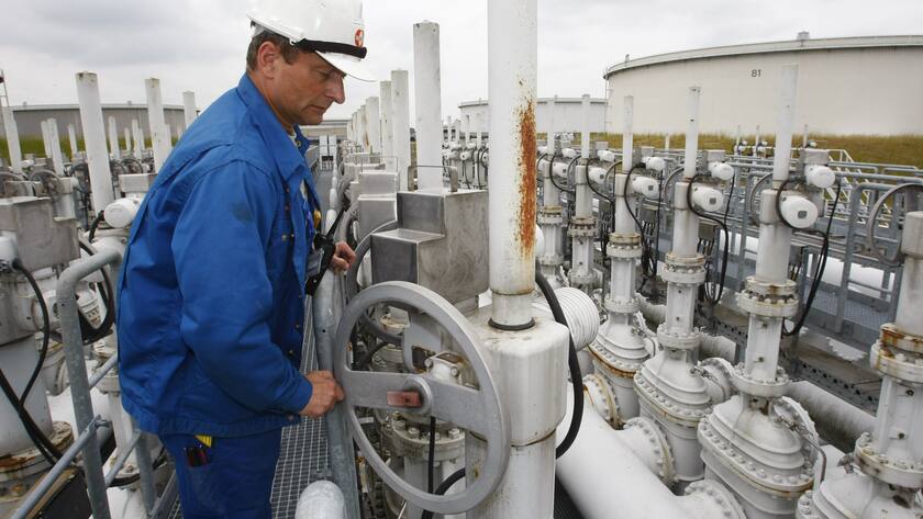 Mann in blauem Overall und weissem Helm dreht an Rad auf einer Erdöl-Raffinerie in Deutschland.