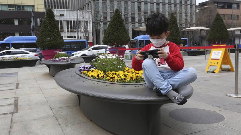 A boy wearing a face mask against the new coronavirus plays with a smartphone in Seoul, South Korea, Thursday, March 26, 2020. For most people, the new coronavirus causes mild or moderate symptoms, such as fever and cough that clear up in two to three weeks. For some, especially older adults and people with existing health problems, it can cause more severe illness, including pneumonia and death. (AP Photo/Ahn Young-joon)