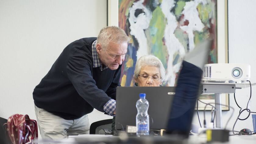 er Pro Senectute Kursleiter gibt Senioren Hilfestellung waehrend des "Windows - Grundkurs Laptop"