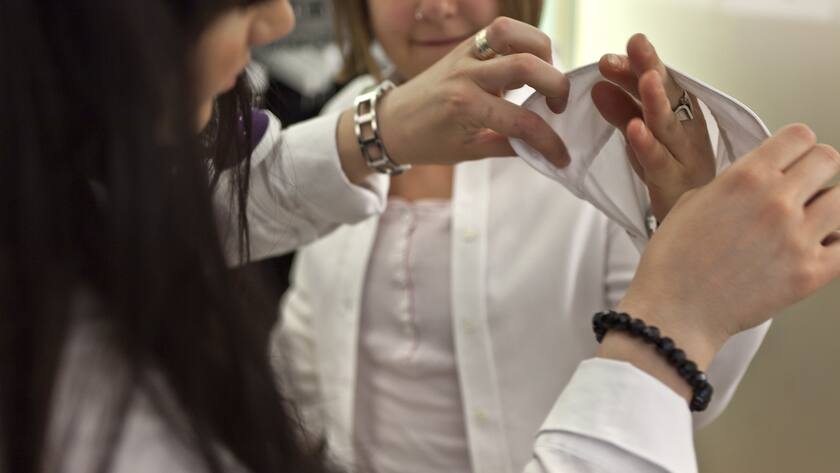 Eine Frau probiert mit Hilfe einer Verkäuferin im Modehaus Schild eine Bluse an.