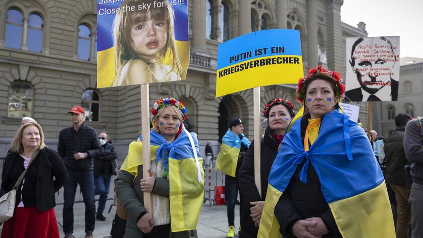 Protesters wear Ukrainian flags and hold banners during a demonstration against the Russian invasion of Ukraine in front of the Swiss parliament building in Bern, Switzerland, Saturday, March 19, 2022. (KEYSTONE/Peter Klaunzer)