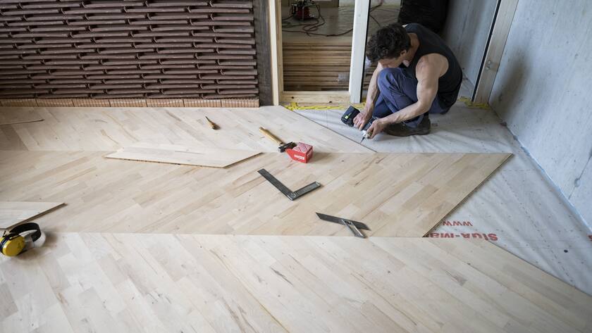Ein Arbeiter verlegt im Forschungs- und Innovationsgebäude NEST der Empa einen Parkettboden.