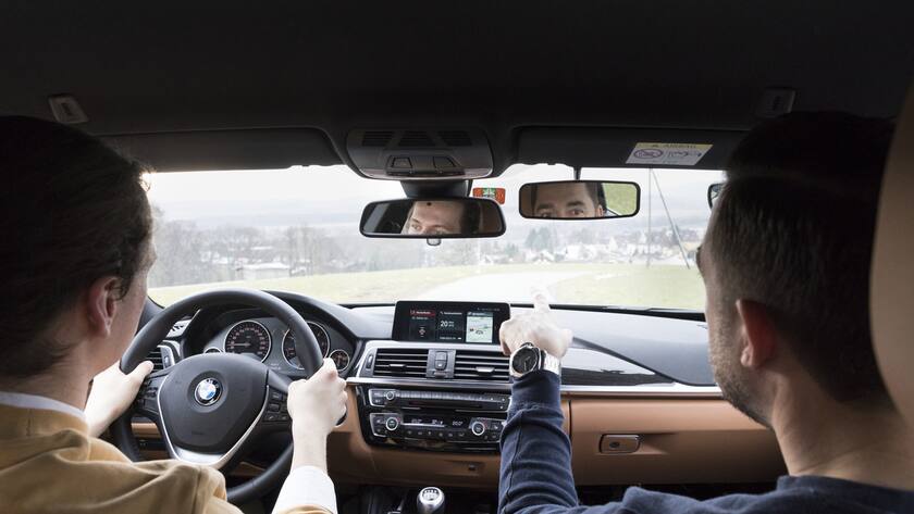 Zwei Personen fahren in einem BMW einer Schweizer Landstrasse entlang.