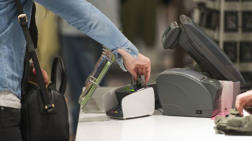 Eine Frau hält eine Plastikkarte an einen Kartenleser in einem Laden.