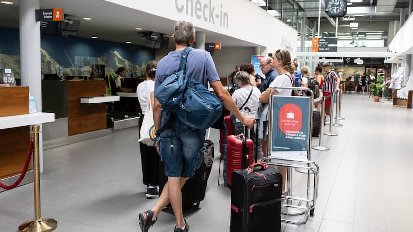 Fluggäste warten am Check-in Schalter in Zürich mit ihrem Gepäck.
