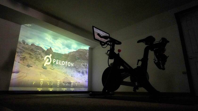 A projection of a desert scene is casted onto a wall near a Peloton fitness bike in a basement home gym, Tuesday, Sept. 15, 2020, in Lutherville-Timonium. Home gyms have picked up in 2020 with sales of exercise bikes going up during the COVID-19 pandemic. (AP Photo/Julio Cortez)