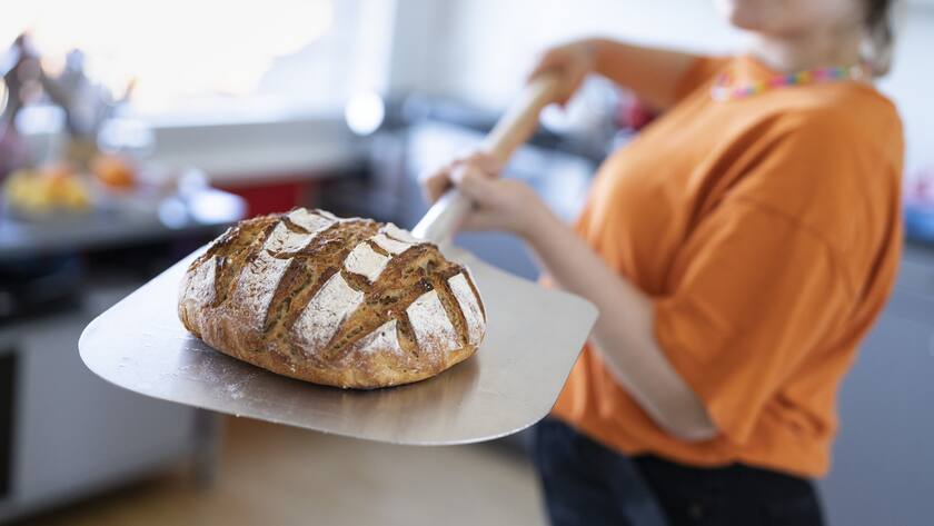 Eine junge Frau nimmt einen Laib selbstgebackenes Brot aus dem Ofen, fotografiert am 24. Maerz 2021 in Zuerich. (KEYSTONE/Gaetan Bally)