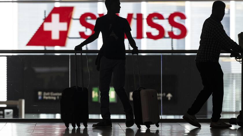Menschen warten am Flughafen auf ihren Abflug in die Ferien. Dahinter das Swiss-Logo.