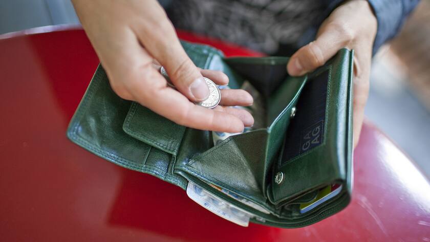 Hand einer Frau hält Münzen in der Hand über offenem Portemonnaie.