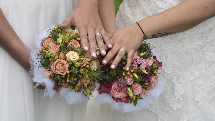 Hände zweier Bräute mit Eheringen und Strauss.