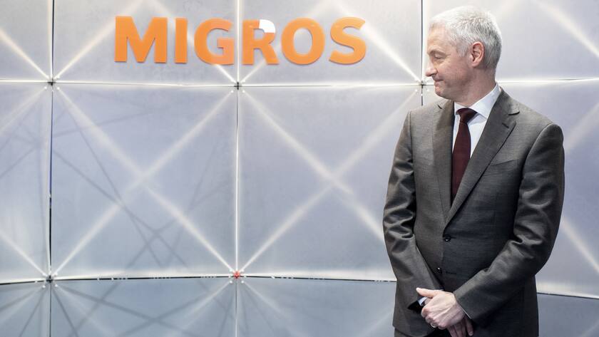 Fabrice Zumbrunnen steht neben dem Migros-Logo und schaut seitlich darauf.