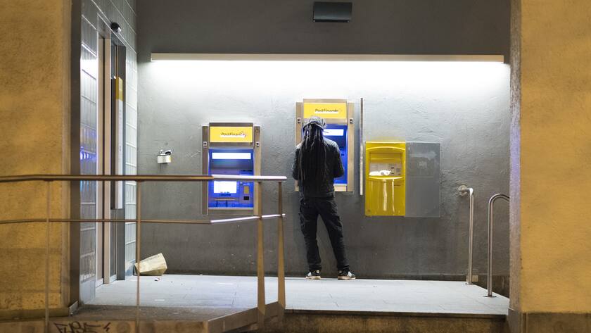 Mann von hinten im halbdunklen an Postfinance-Schalter.