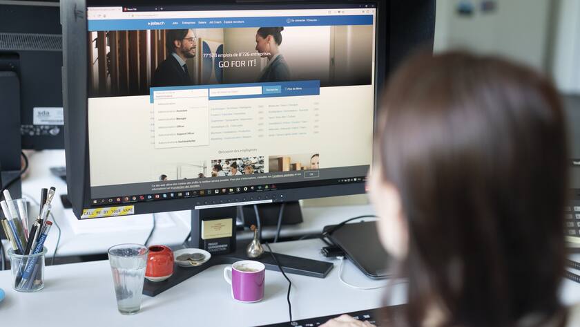 Frau von hinten an PC schaut Job.ch Plattform an.