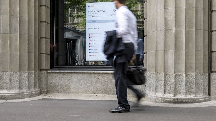 Auf einem Bildschirm im Fenster der UBS Filiale an der Zürcher Bahnhofstrasse werden Börsendaten angezeigt. Ein Mann in weissem Hemd geht daran vorbei.