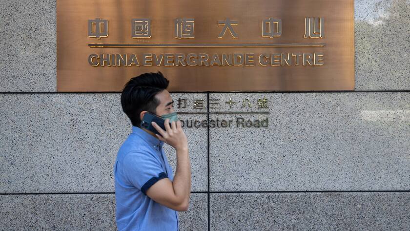 Mann am Handy geht an einer Messing Tafel mit Evergrande Aufschrift an Hauswand vorbei.