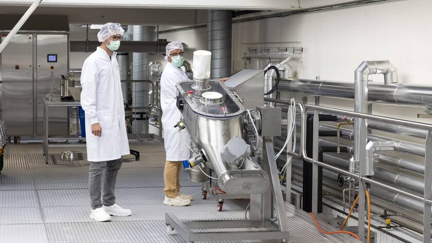 Zwei Männer in weissen Kitteln mit Haube und Maske in einer Nestlé-Nahrungsmittelfabrik.