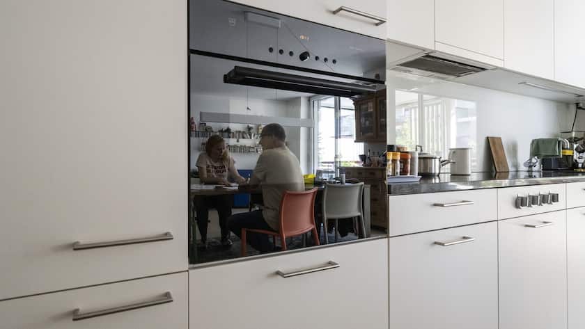 m Backofenglas spiegelt sich eine Familie am Esstisch im Wohnzimmer ihrer Wohnung