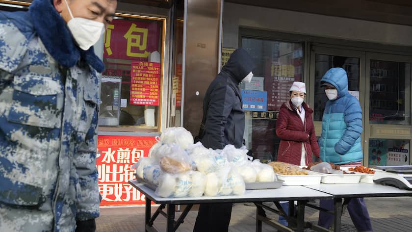 Residents pass by an outdoor stand selling food in Beijing, Thursday, Dec. 15, 2022. A week after China eased some of the world's strictest COVID-19 containment measures, uncertainty remains over the direction of the pandemic in the world's most populous nation. (AP Photo/Ng Han Guan)