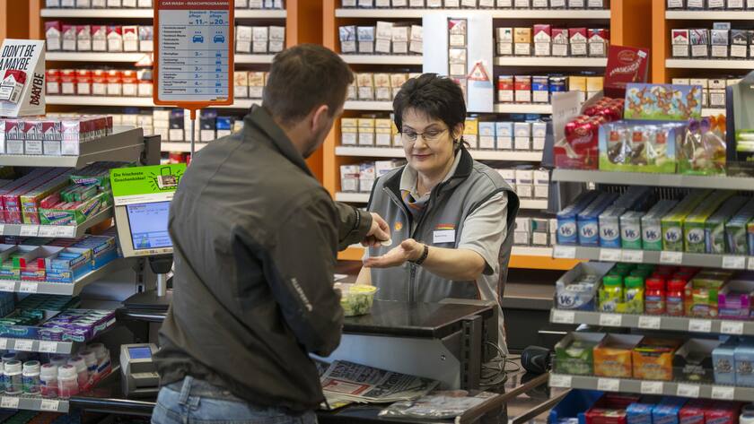 Ein Mann bezahlt an der Kasse eines Migrolino-Shops mit Münzen.