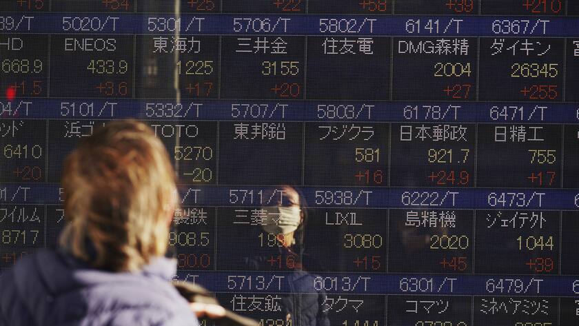 A woman wearing a protective mask looks at an electronic stock board showing Japan's Nikkei 225 index at a securities firm on the first trading day of the year Tuesday, Jan. 4, 2022, in Tokyo. (KEYSTONE/AP Photo/Eugene Hoshiko)