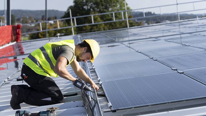Ein Solateur der Firma IngEne steckt Stromkabel der neuen mit Solarpanels auf dem Dach des Eisfeldes der Winter und Sports World Wallisellen zusammen