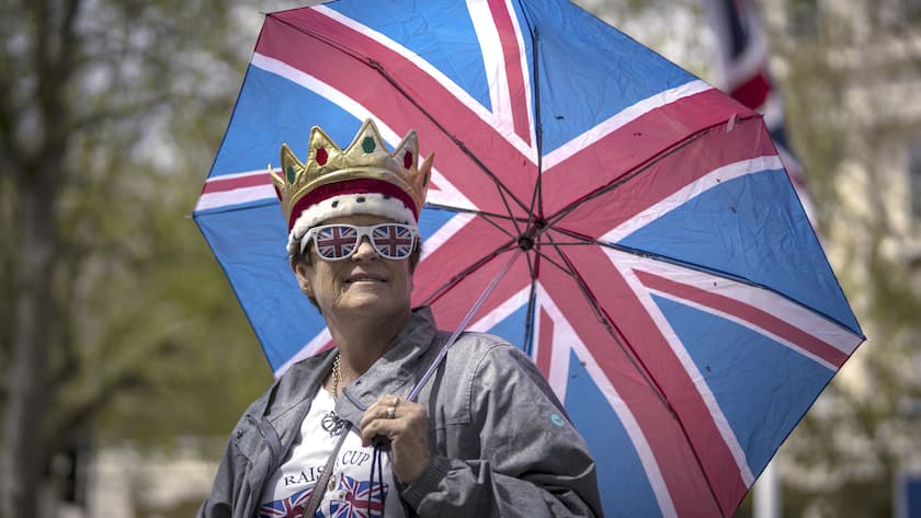 A royal fan holds and umbrella, waiting along the King's Coronation route at The Mall in London, Friday, May 5, 2023. The Coronation of King Charles III will take place at Westminster Abbey on May 6. (AP Photo/Emilio Morenatti)