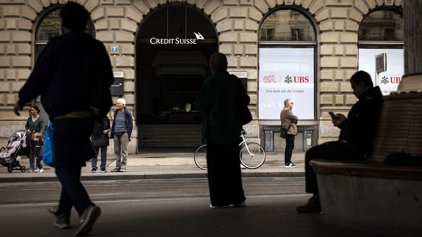 People stand in front of a logo of Swiss bank Credit Suisse next to a screen showing a logo of Swiss Bank UBS and the logo of Swiss Football Association SFV with the words "A bank like Switzerland" at Zurich's Paradeplatz on Monday, June 10, 2024 in Zurich, Switzerland. (KEYSTONE/Michael Buholzer)