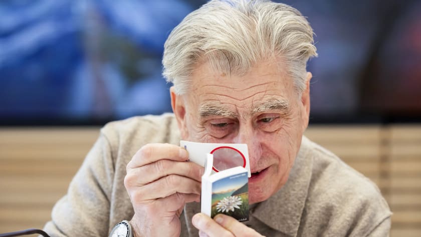 Nick Hayek, CEO Swatch Group AG, looks at the annual report with a magnifying glass, prior to a press conference to present the annual results for 2024, Wednesday, March 19, 2025, in Biel, Switzerland. (KEYSTONE/Peter Klaunzer)