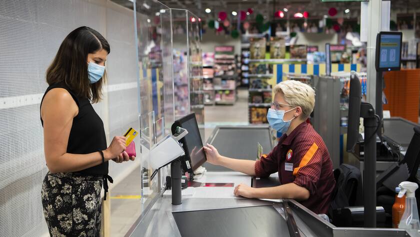 Une personne paie des courses a la caisse a une vendeuse portant un masque sur le visage dans un magasin Migros le mercredi 8 juillet 2020 a Crissier. Les masques sont obligatoires dans les magasins des 10 personnes dans le canton de Vaud a partir d'aujourd'hui. (KEYSTONE/Jean-Christophe Bott)