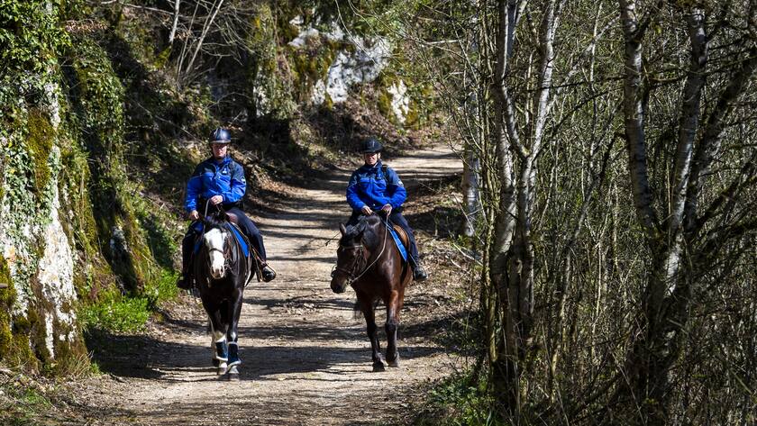 Une patrouille equestre de la police jurassienne, circule le long de la riviere Le Doubs pour veiller a l'application des mesures protectrices contre le Coronavirus (Covid-19) le samedi 4 avril 2020 a Saint-Ursanne dans le Jura. (KEYSTONE/Jean-Christophe Bott)