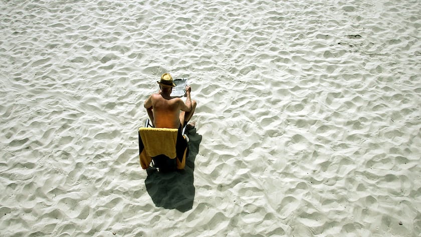 Von viel Sand umgeben sitzt dieser Mann alleine an einem Strand. Luftaufnahme.