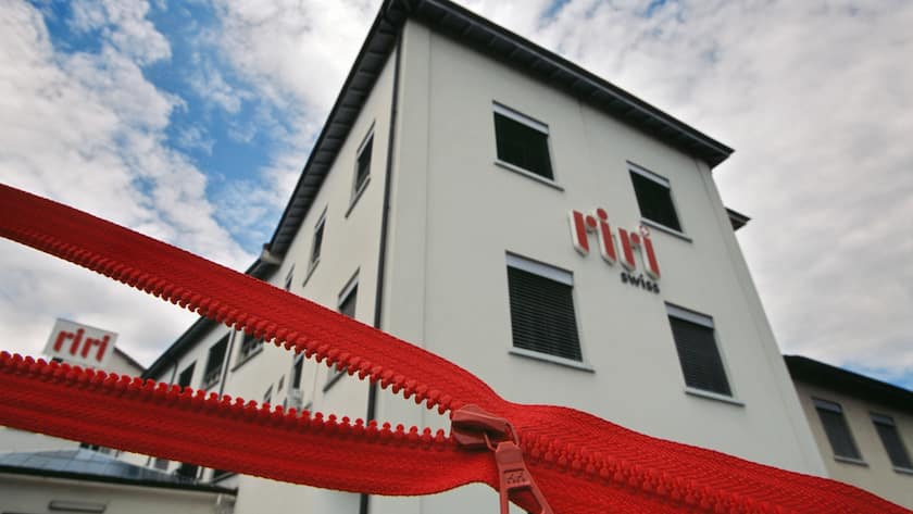 Halbgeöffnetes rotes Reissverschlusssband vor Gebäude von Riri.