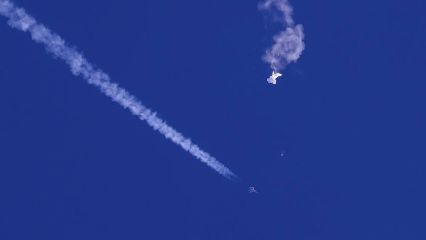 In this photo provided by Chad Fish, the remnants of a large balloon drift above the Atlantic Ocean, just off the coast of South Carolina, with a fighter jet and its contrail seen below it, Saturday, Feb. 4, 2023.