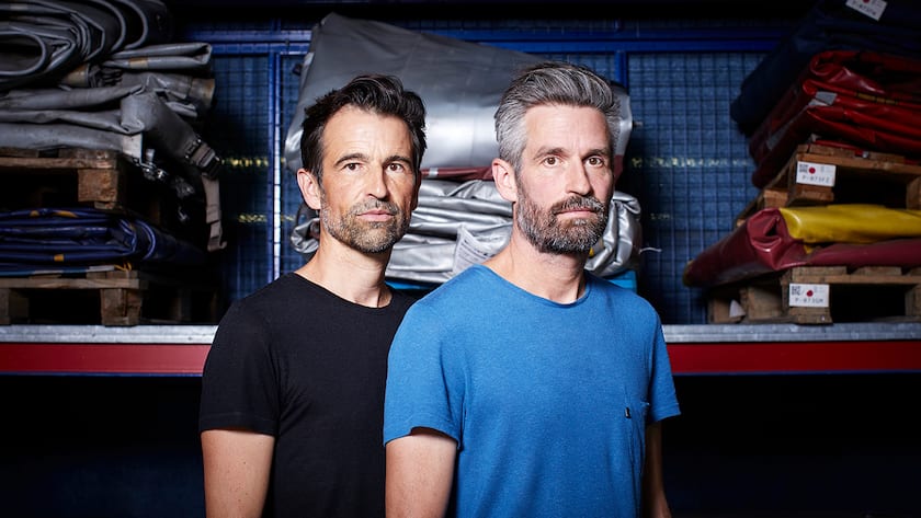 Daniel Freitag (links) und Markus Freitag (rechts) vor einem Regal mit LKW-Planen, in ihrem Hauptsitz in Zürich Oerlikon.