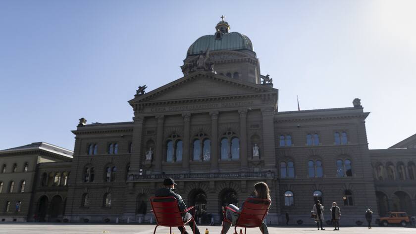 Zwei Jugendliche geniessen die Sonne auf dem Bundesplatz vor dem Parlamentsgebaeude, wo am Nachmittag die Fruehlingssession der Eidgenoessischen Raete beginnt, am Montag, 1. Maerz 2021 in Bern. (KEYSTONE/Alessandro della Valle)