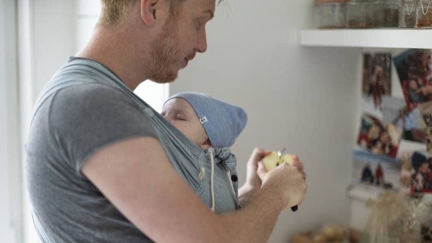Ein Vater bereitet an seinem freien Tag zu Hause das Fruehstuck zu waehrend er seinen vier Montate alten Sohn im Tragetuch traegt, fotografiert am 15. Mai 2020 in Aarau. (KEYSTONE/Gaetan Bally)
