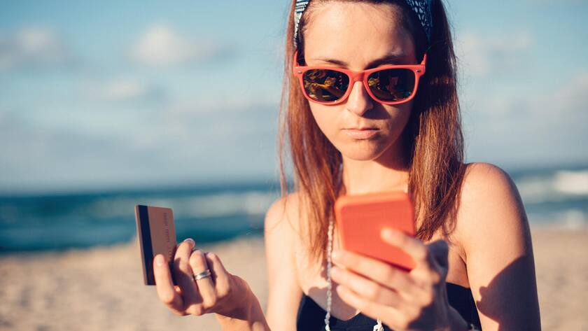 Young woman on the beach phoning the bank for credit card support