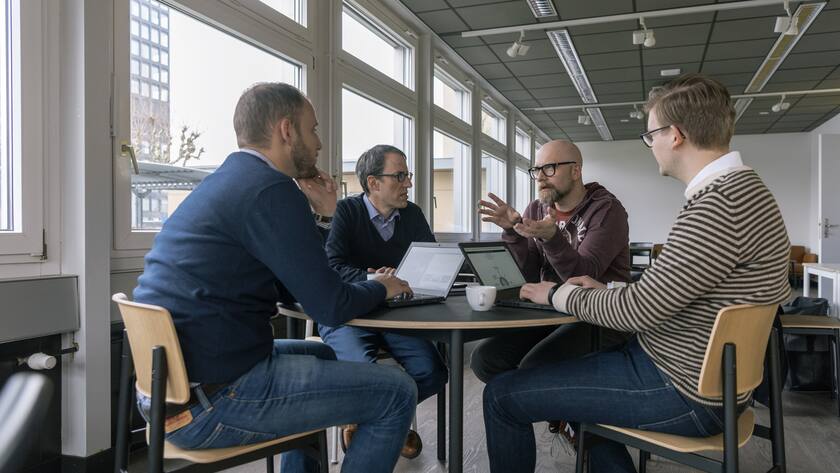 Eine Gruppe von vier Männern sitzt beim Gespräch um einen runden Tisch in den Zuger Crypto Valley Labs.